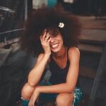 Cheerful woman wearing ripped jeans and curly hair with flower, enjoying a sunny day outdoors.